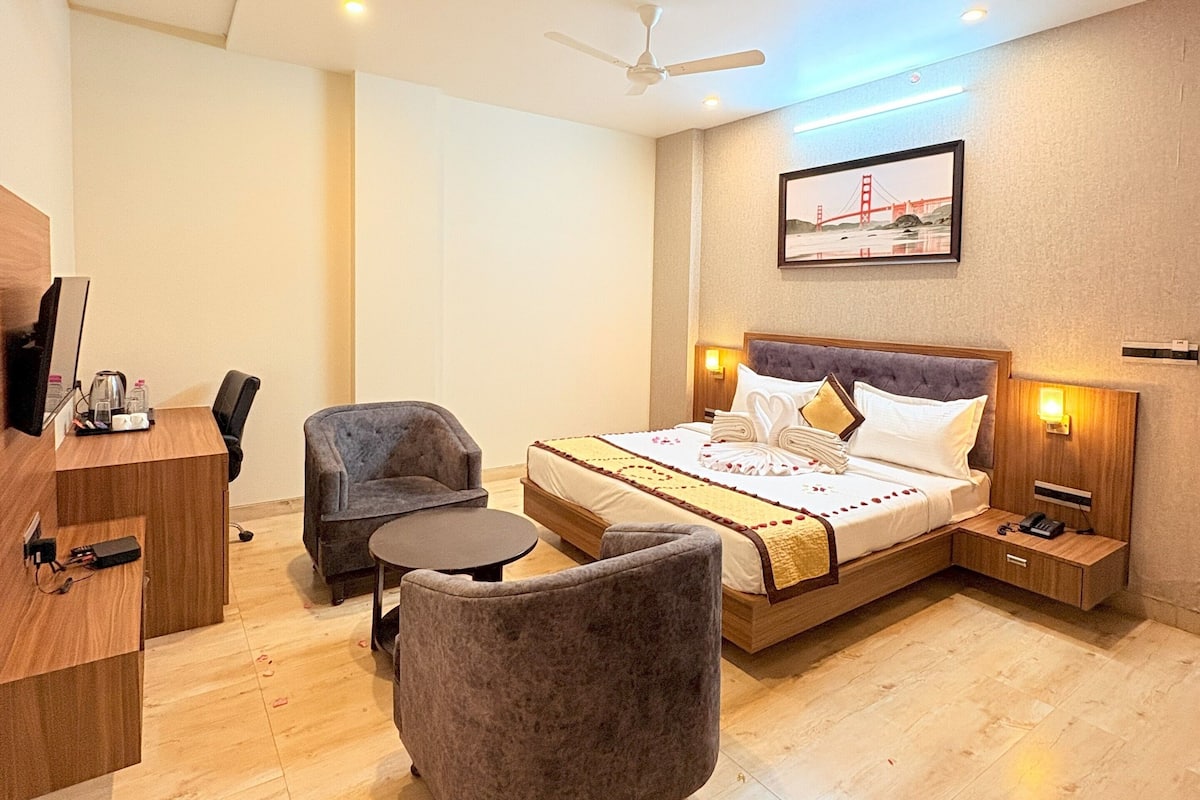A hotel room with a bed, a desk, a chair, a small table, and a ceiling fan.
