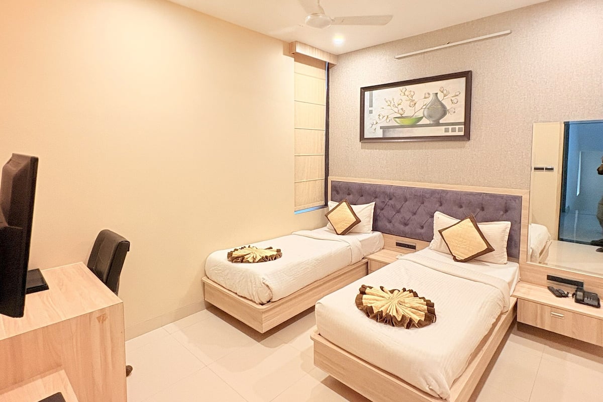 A hotel room with two beds, a desk, a chair, a ceiling fan, and a painting on the wall.