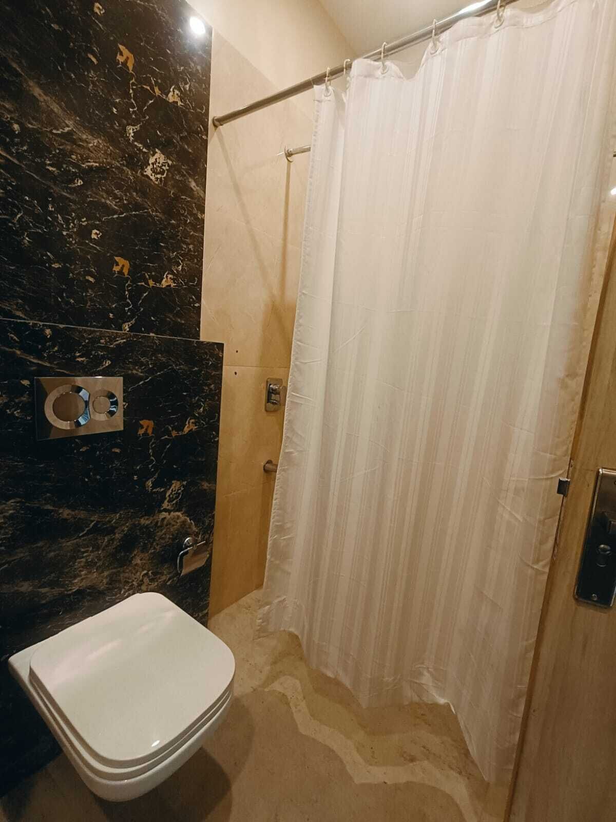 A bathroom with a marble wall, a white toilet, a shower curtain, and a metal towel rack.