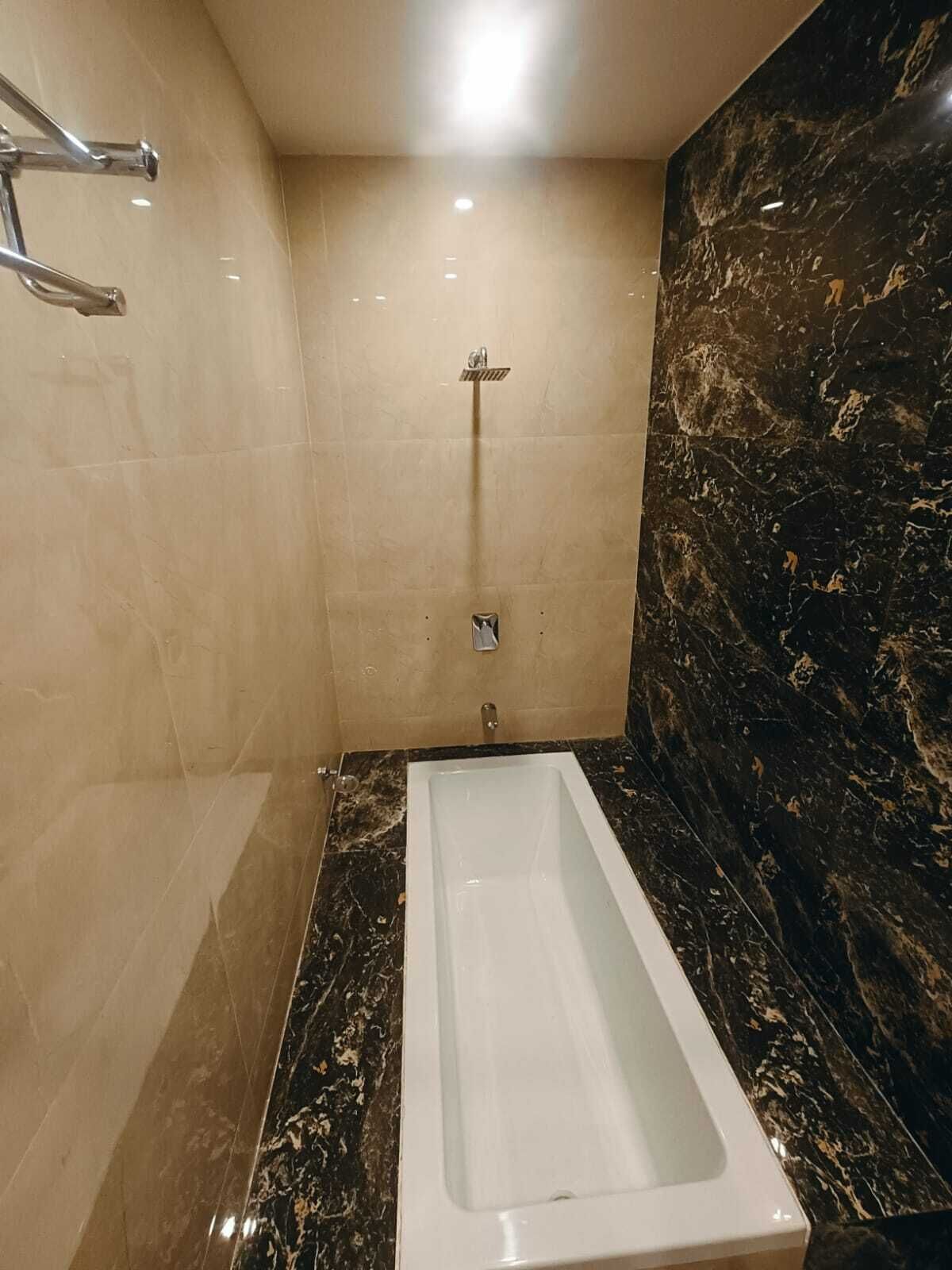 Een badkamer met een rechthoekig bad, beigekleurige betegelde muren en een marmeren spatwand.