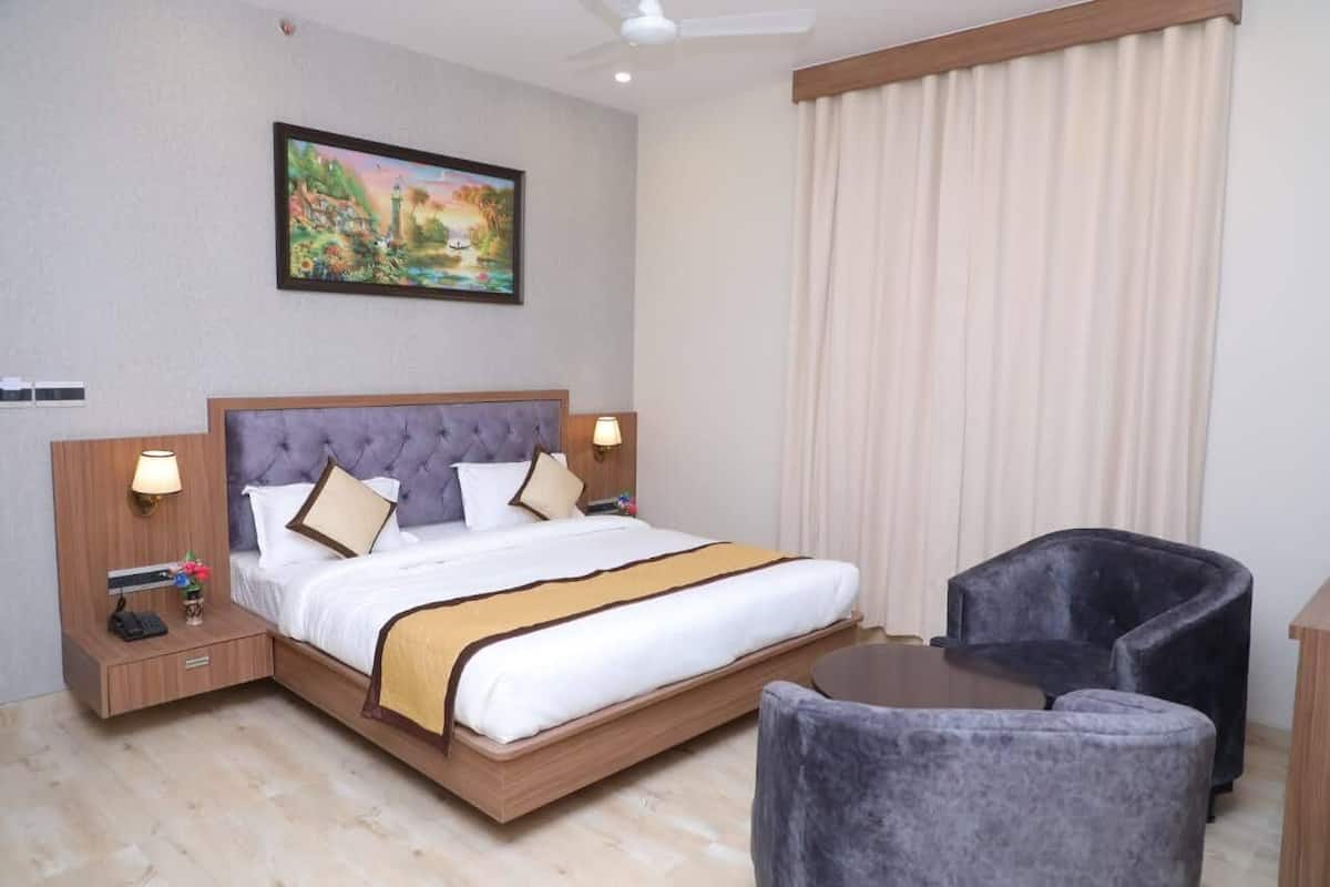 A hotel room with a large bed, two bedside lamps, a nightstand, a chair, a small table, and a painting on the wall.