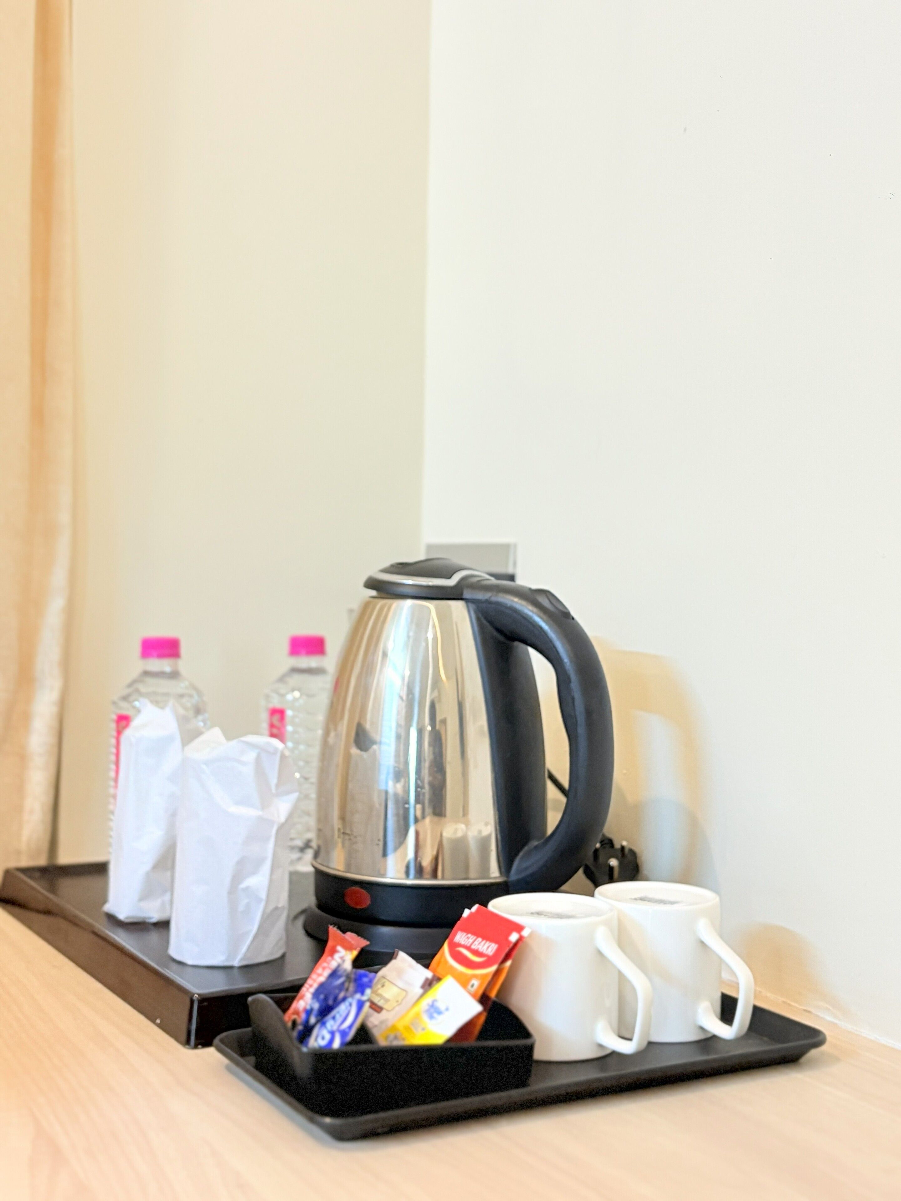 A tray with a coffee maker, two bottles of water, a white mug, and some snacks.