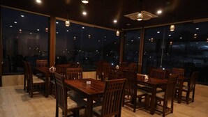 A restaurant with wooden tables and chairs, large windows, and hanging lights. - Parampara Hotels And Resorts (Udaipur)
