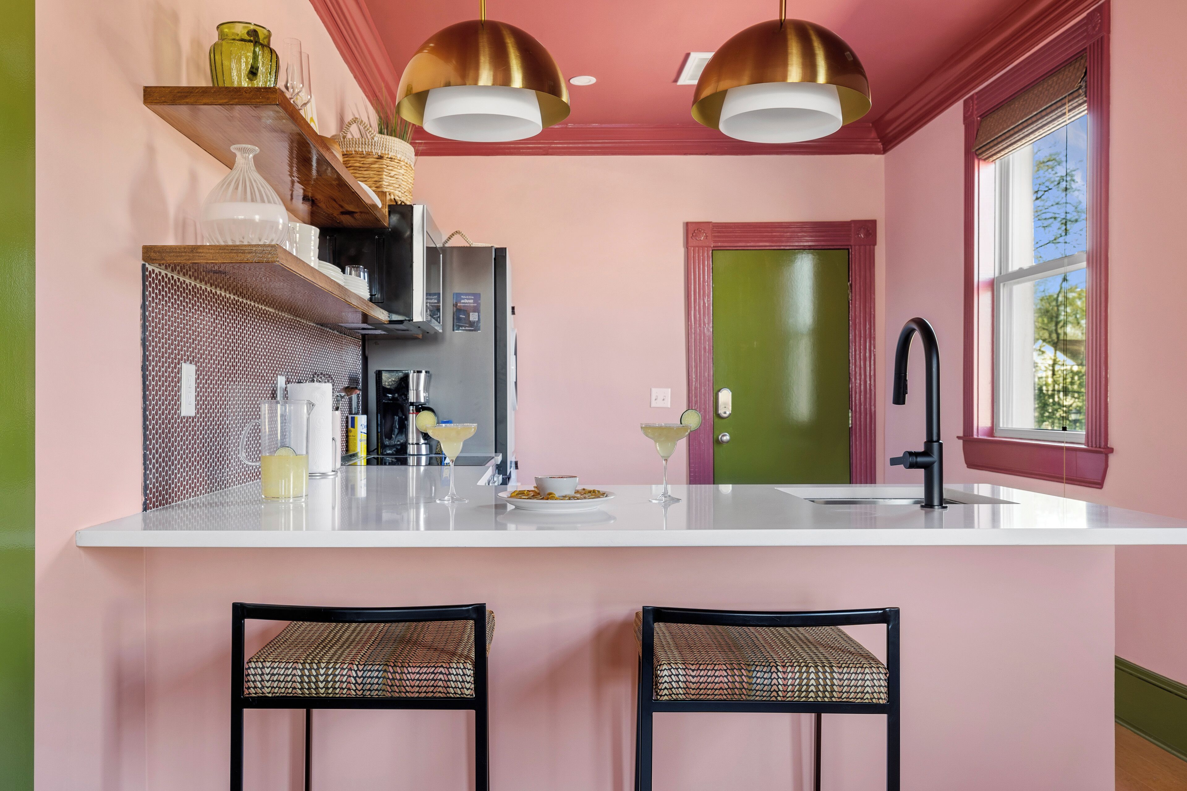 A kitchen with a white countertop, two black chairs, a green door, and a window with a view.