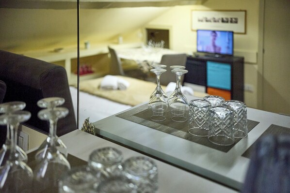Une chambre d’hôtel avec un lit, une télévision et une petite table avec des verres à vin et des verres à eau.