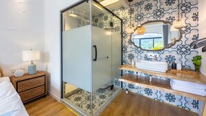 A bathroom with a glass shower enclosure, a sink with a mirror above it, and a patterned wall.
