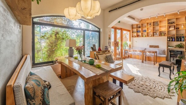 A spacious living area with a large window, a wooden dining table, and a cozy seating arrangement.
