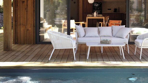 A wooden deck with a pool, white outdoor furniture, and a glass door leading to an interior space.