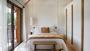A modern bedroom with a large bed, a bench, and a view of the outdoors.