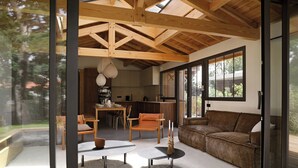 A modern interior with a wooden ceiling, a dining area with chairs, a sofa, and a kitchen in the background.