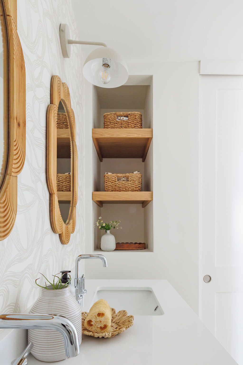 A bathroom with a white sink, a mirror, a light fixture, and wooden shelves with baskets.
