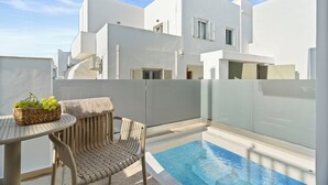 A modern white building with a glass-enclosed pool area, wicker furniture, and a wicker basket with grapes. - Dream of Paros by GHH (Paros)