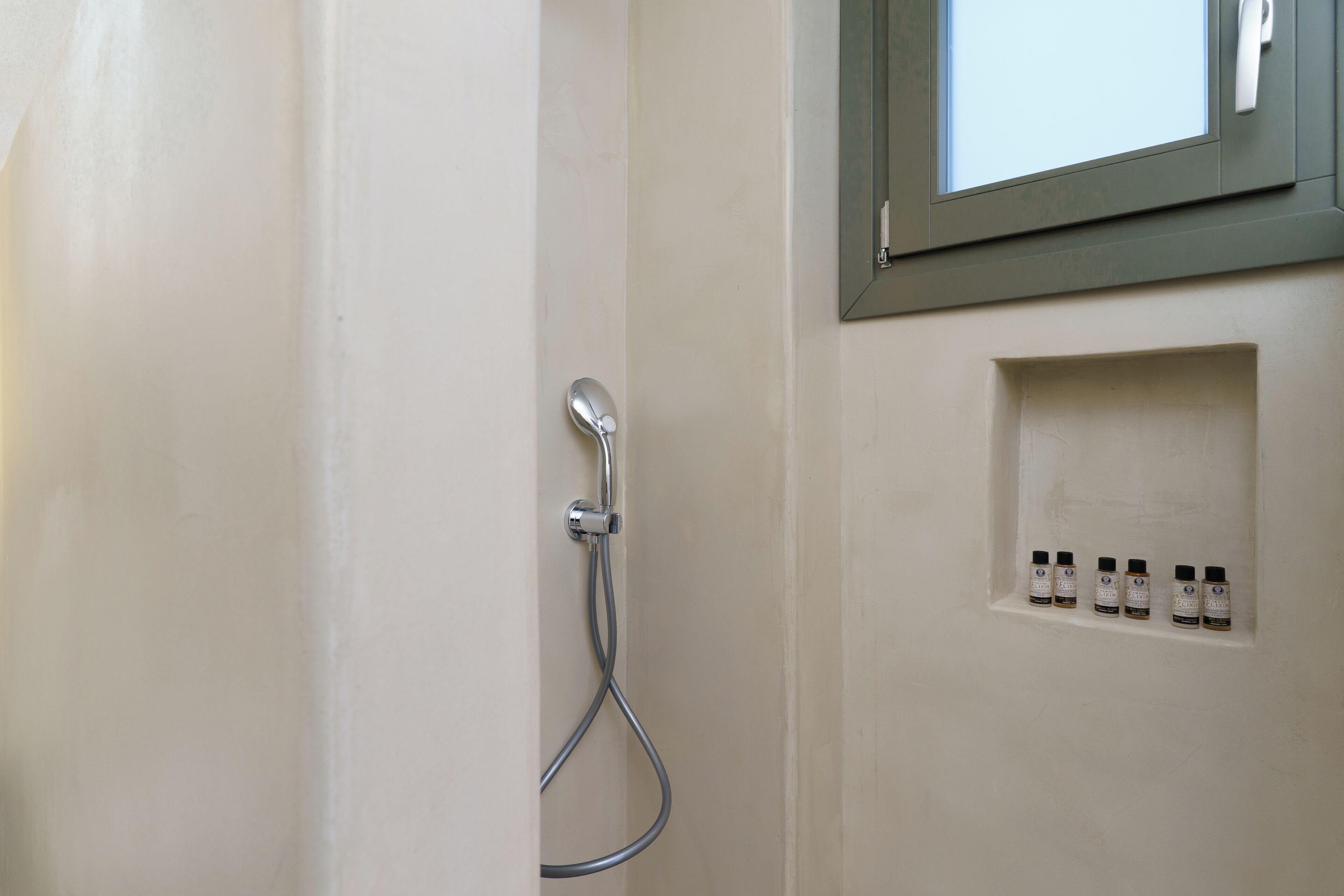 A bathroom with a shower, a window, and a shelf with toiletries.