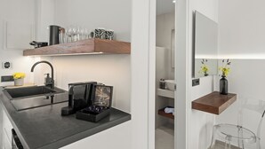 A modern kitchen with a black countertop, a sink, and a coffee machine. There are clear glass chairs and a wooden shelf with decorative items. - Dream of Paros by GHH (Paros)
