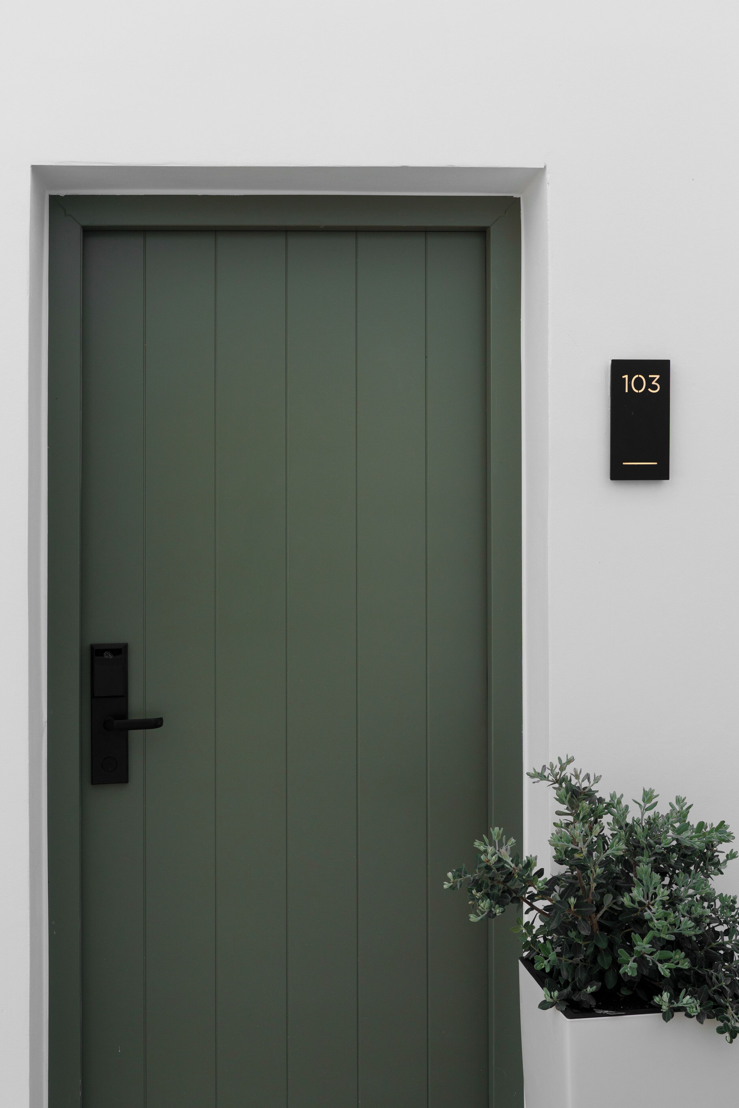 Una puerta verde con un pomo negro y una pequeña placa negra con el número 103.