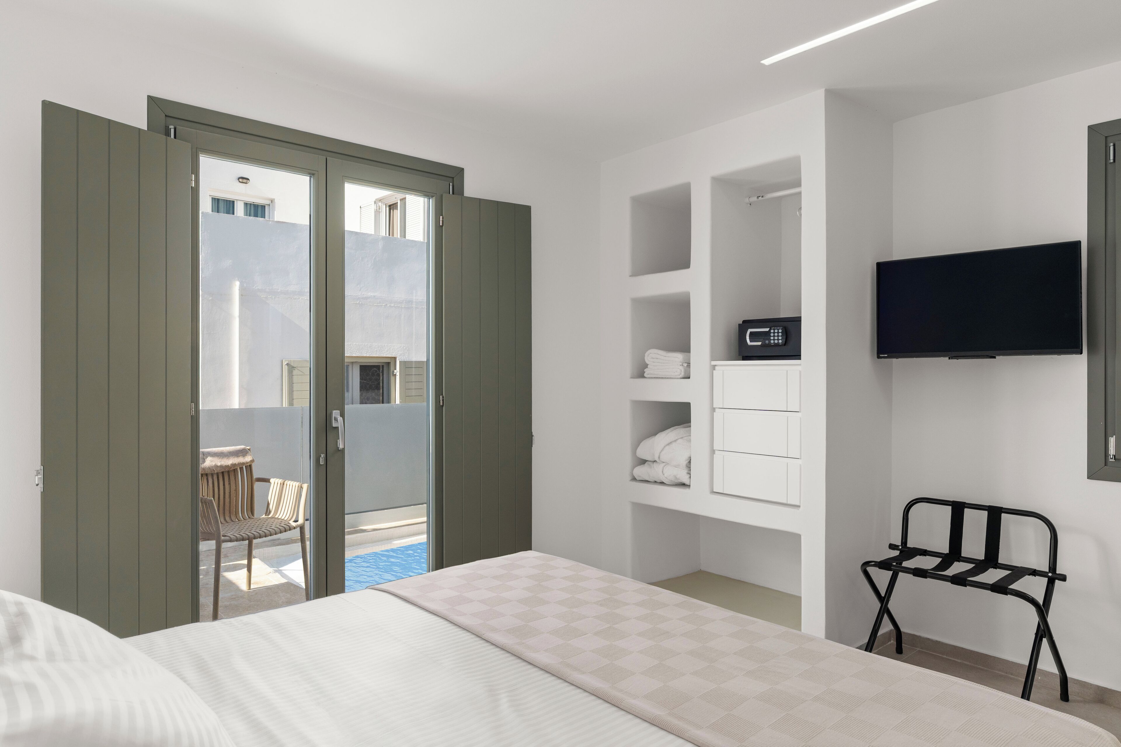 A hotel room with a bed, a TV, a chair, and a balcony with a chair.