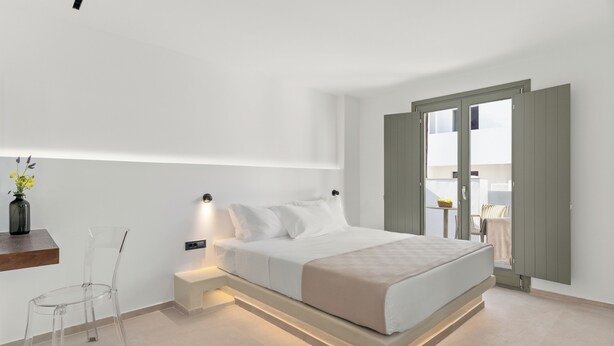 A modern bedroom with a bed, bedside table, and a clear chair. - Dream of Paros by GHH (Paros)