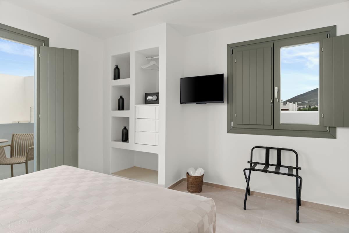 A modern bedroom with a bed, a TV, a chair, and a window with a view.