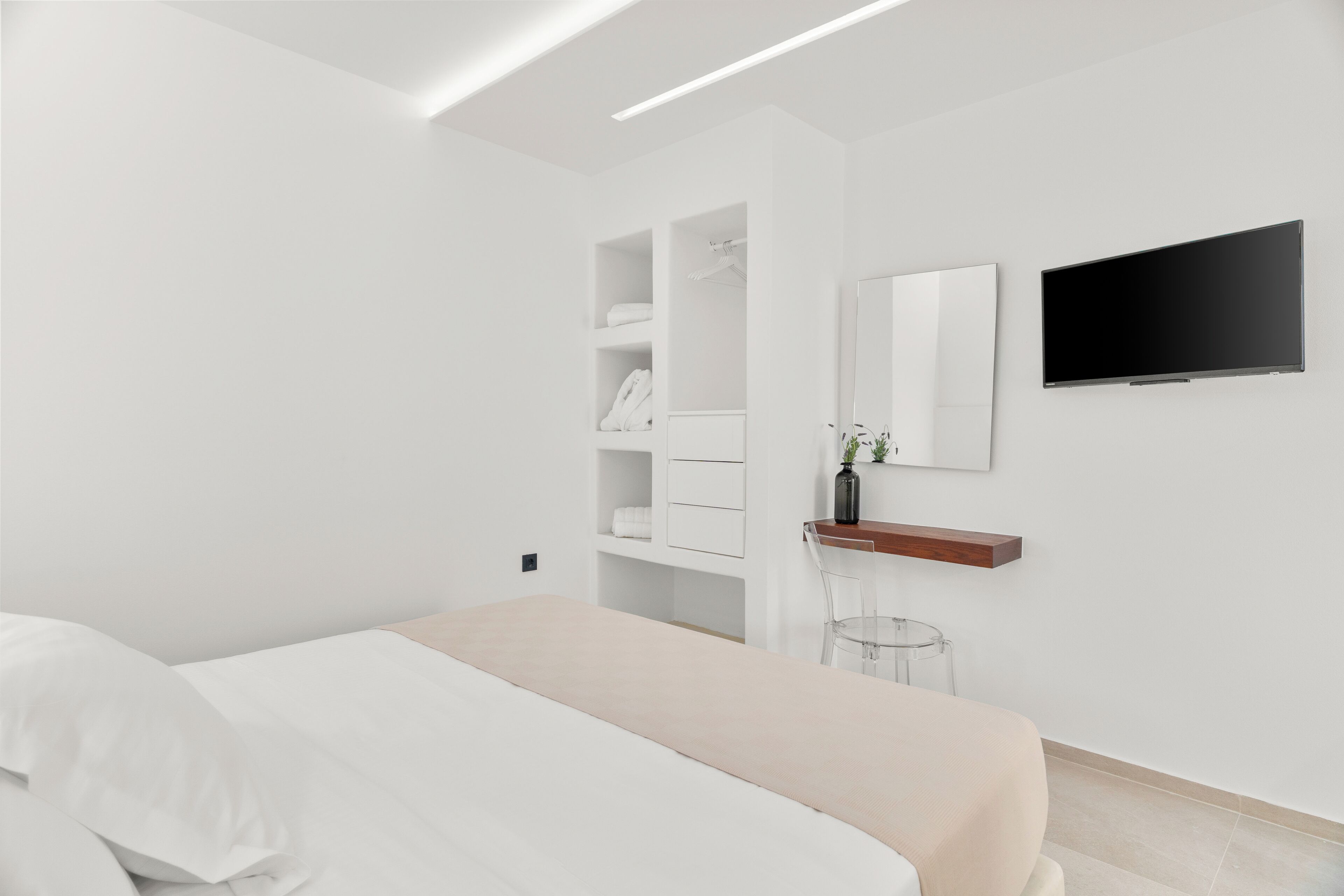 A modern bedroom with a bed, built-in wardrobe, a mounted TV, and a small side table.