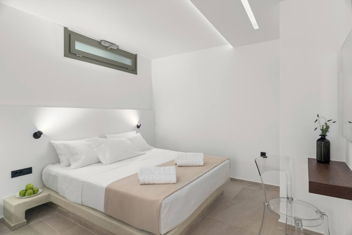 A modern bedroom with a bed, bedside table, and a clear chair.