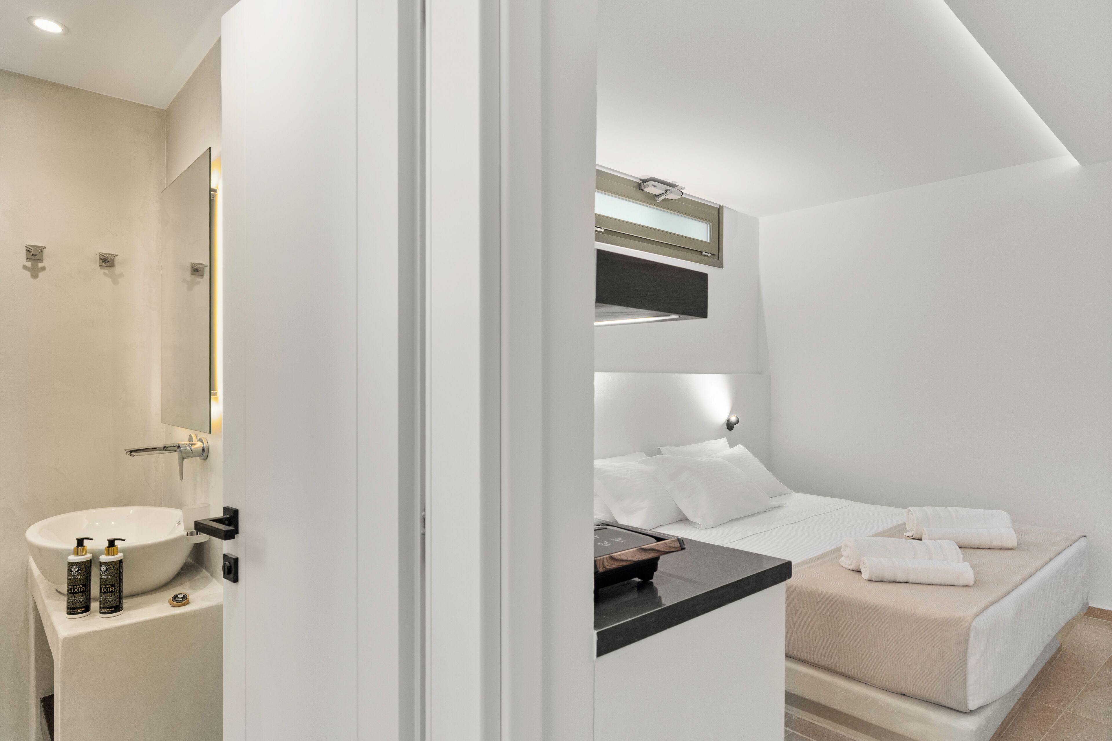 A modern hotel room with a large white sink, a bed with beige bedding, and a small bedside table.