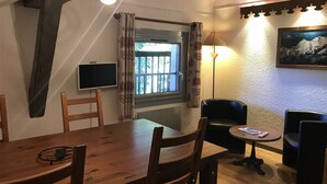 Un comedor con una mesa y sillas de madera, una mesita redonda con una lámpara, y una ventana con cortinas.
