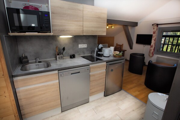 A compact kitchen with a microwave, dishwasher, and sink. There is a small window with a view of greenery outside.