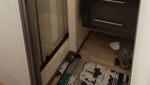 Un baño moderno con cabina de ducha de vidrio, tocador de madera con espejo y alfombra estampada en el suelo.