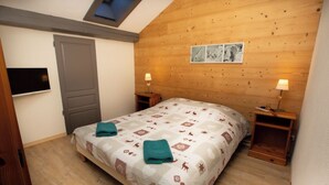 Un dormitorio con techo de madera, una cama con colcha estampada, dos mesitas de noche con lámparas y una puerta.