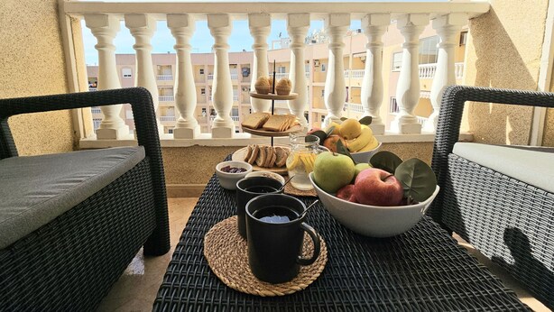 Un balcon agrémenté de meubles en osier, une table avec des éléments pour le petit-déjeuner et une vue sur un immeuble doté de balcons.