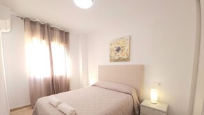 Une chambre à coucher bien rangée, avec un lit, une table de chevet dotée d’une lampe et une œuvre d’art accrochée au mur.