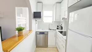 Une cuisine compacte avec des meubles blancs, un lave-vaisselle en acier inoxydable, un four encastré et une petite fenêtre.