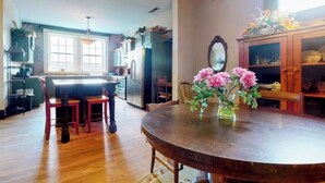 A dining area with a wooden table and chairs, a vase with flowers, and a kitchen in the background.