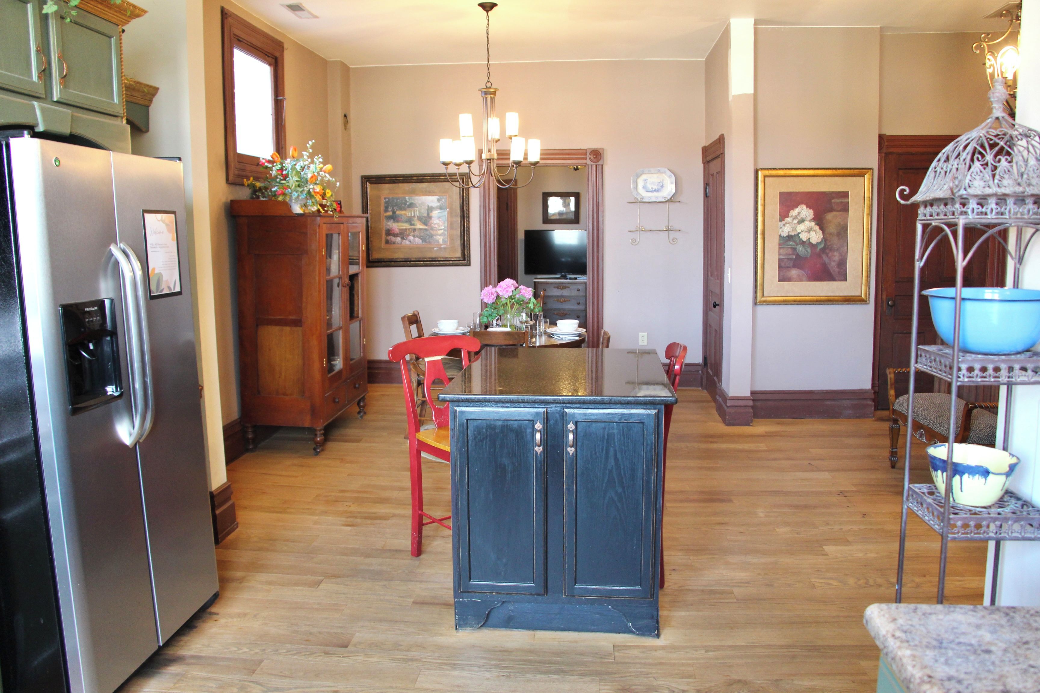 Une cuisine dotée d’un îlot central, de meubles en bois, d’un réfrigérateur, d’une table à manger avec des chaises et d’un lustre.