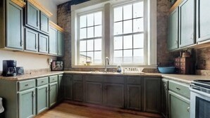 Cocina con gabinetes verdes, un lavamanos doble y una ventana con varios paneles.