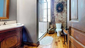 A bathroom with a wooden vanity, a glass shower enclosure, and a rustic brick wall.