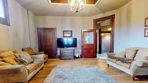 A living room with two sofas, a television, wooden flooring, and a chandelier.