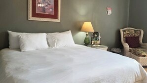A hotel room with a large bed, a framed picture on the wall, a lamp, a chair, and a wall-mounted sign.