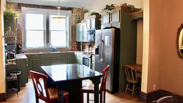 Una cocina con una isla central, armarios verdes, un refrigerador y un comedor con sillas.