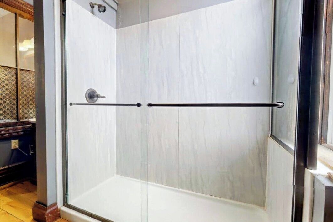 Un espace de douche clos par des parois de verre, avec une barre d’appui en métal.