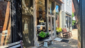 Une devanture de magasin avec un véhicule garé devant, un banc et un bac à fleurs orné de plantes vertes.