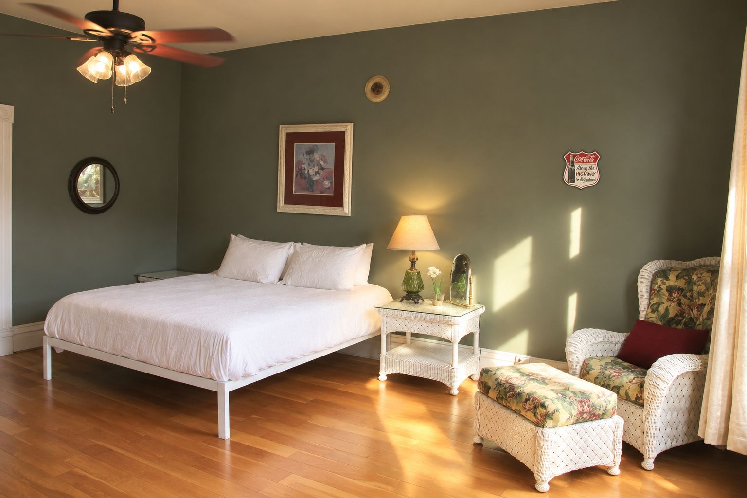 Un dormitorio con cama, mesita de noche, silla, ventilador de techo e imagen colgada en la pared.