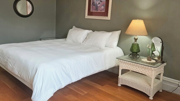A bedroom with a bed, a nightstand, a lamp, a mirror, and a framed picture on the wall.