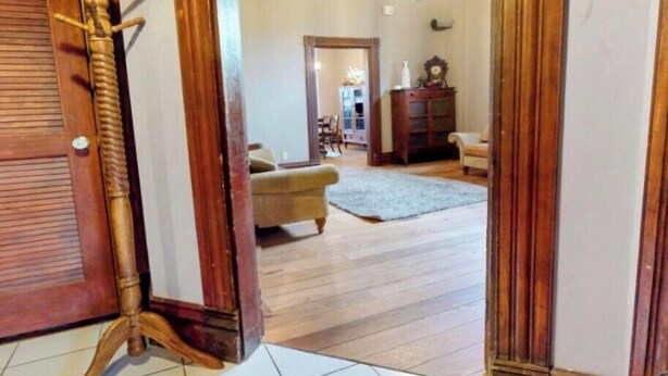 Una puerta de madera con un perchero, una araña y vista a una sala de estar con sofá y alfombra.