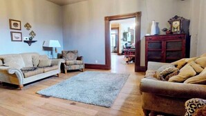 Una sala de estar con un sofá, un sillón y una alfombra. Hay un aparador de madera y un espejo en la pared.