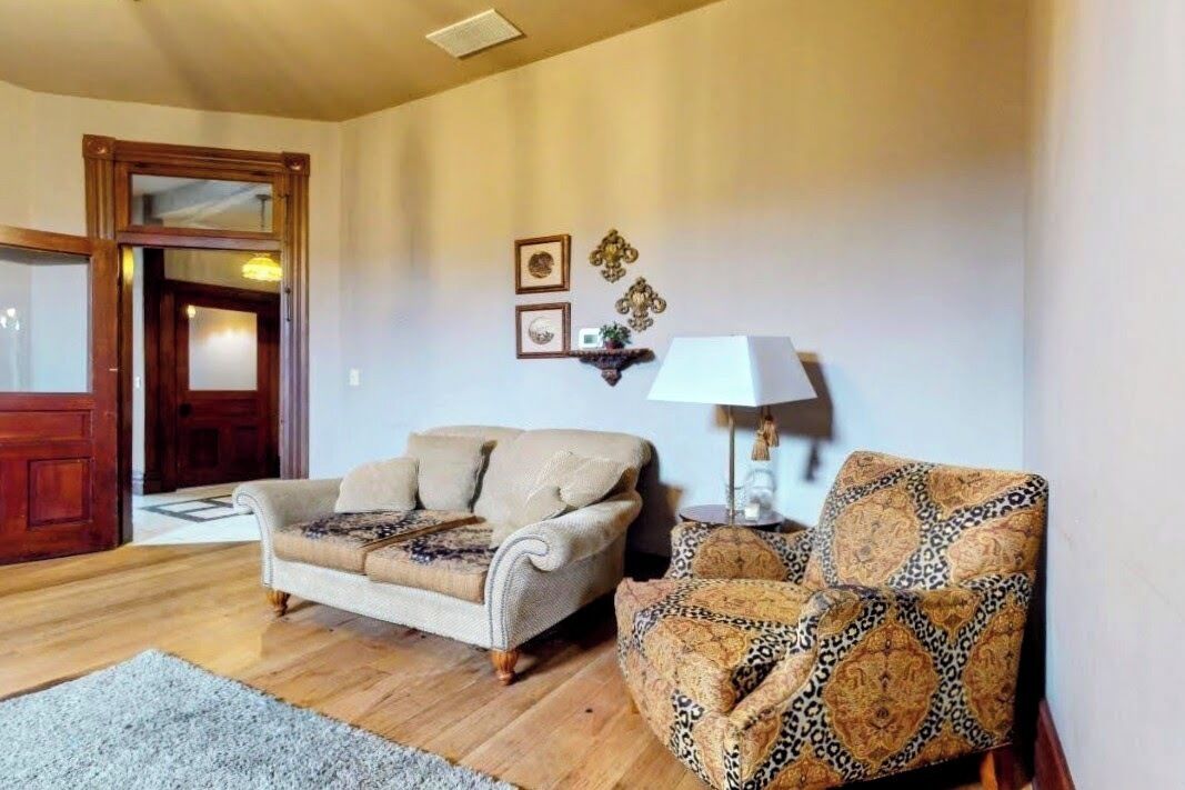 Un salon avec un canapé beige, un fauteuil à motifs, une lampe et un plancher en bois.