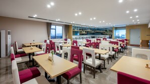 A modern restaurant with multiple tables and chairs, a kitchen area in the background, and large windows allowing natural light. - Lavande Hotel - Huizhou Boluo Shiwan (Huizhou)