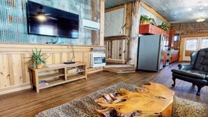 Una sala de estar con una mesa de centro de madera, un televisor de pantalla plana montado en la pared, un refrigerador y un sofá de cuero negro.