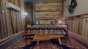 Una habitación de madera con una cama, un banco y una alfombra estampada.