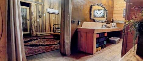Un interior rústic de fusta amb una porta de fusta, una panxa, un rentamans amb armaris d'emmagatzematge i un mirall decoratiu a la paret.